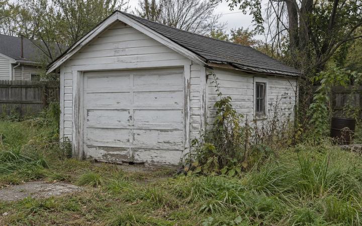 A weathered detached garage with a sagging roofline in an overgrown yard