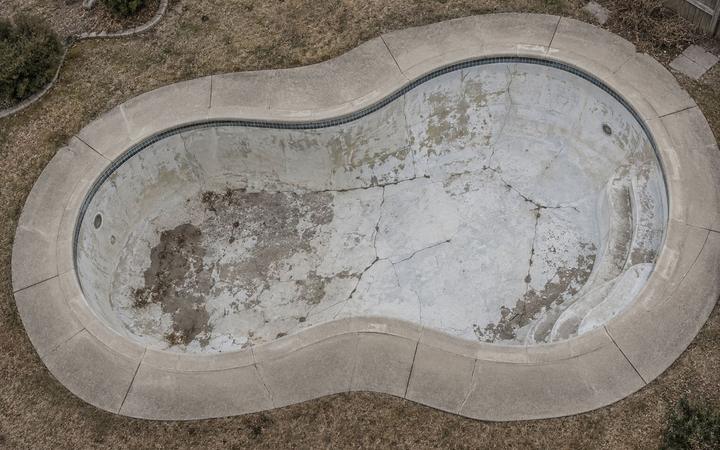 An empty cracked in ground swimming pool seen from above