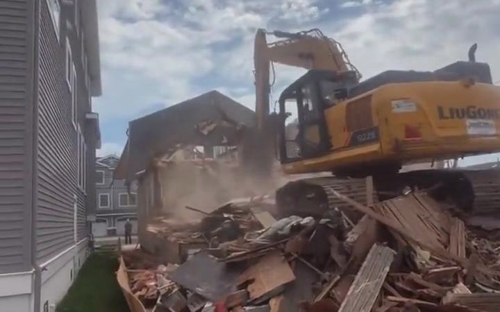 An excavator taking down a house beside an occupied neighbor