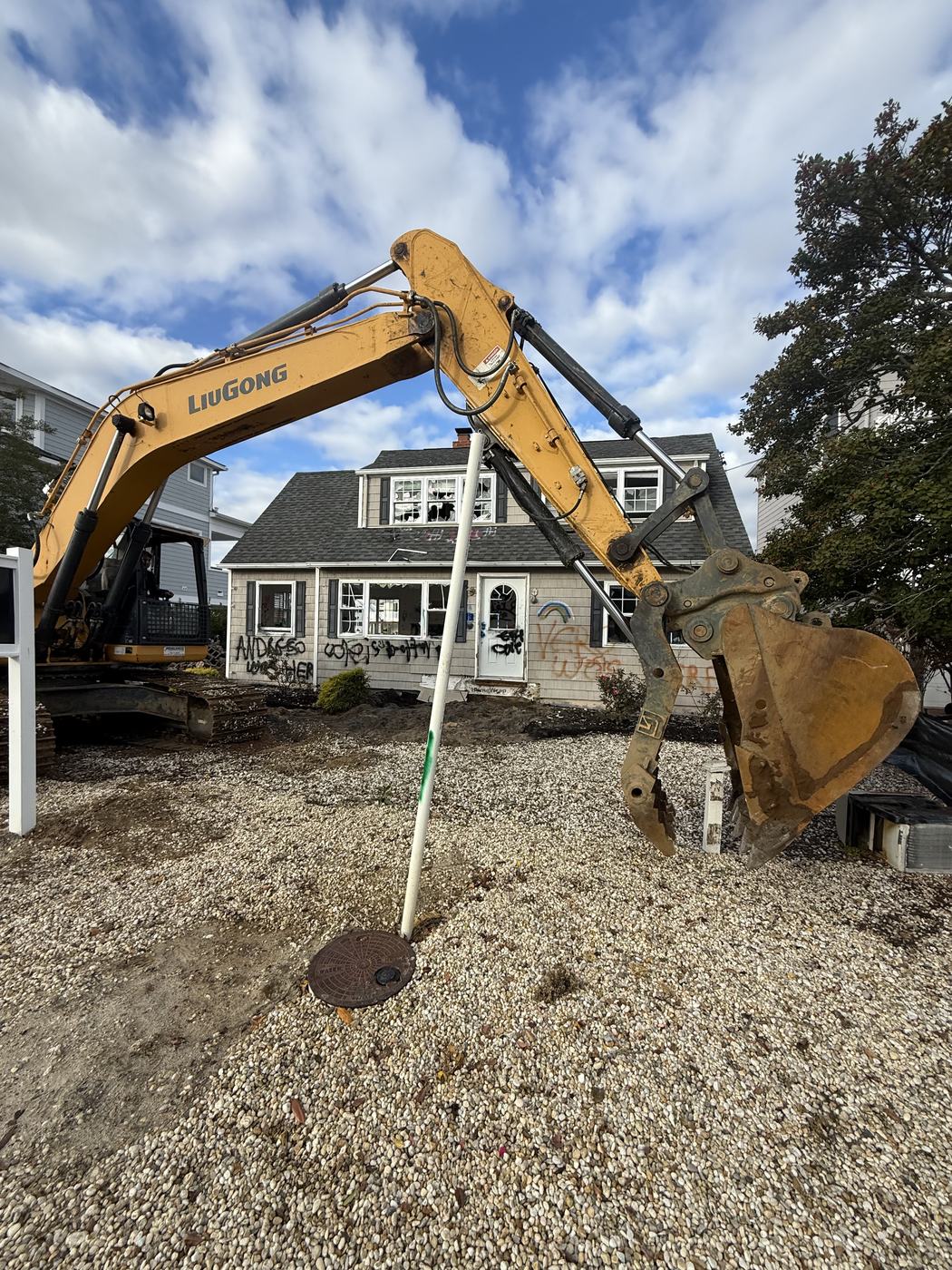 A vacant tagged house with broken windows before demolition, excavator staged in front
