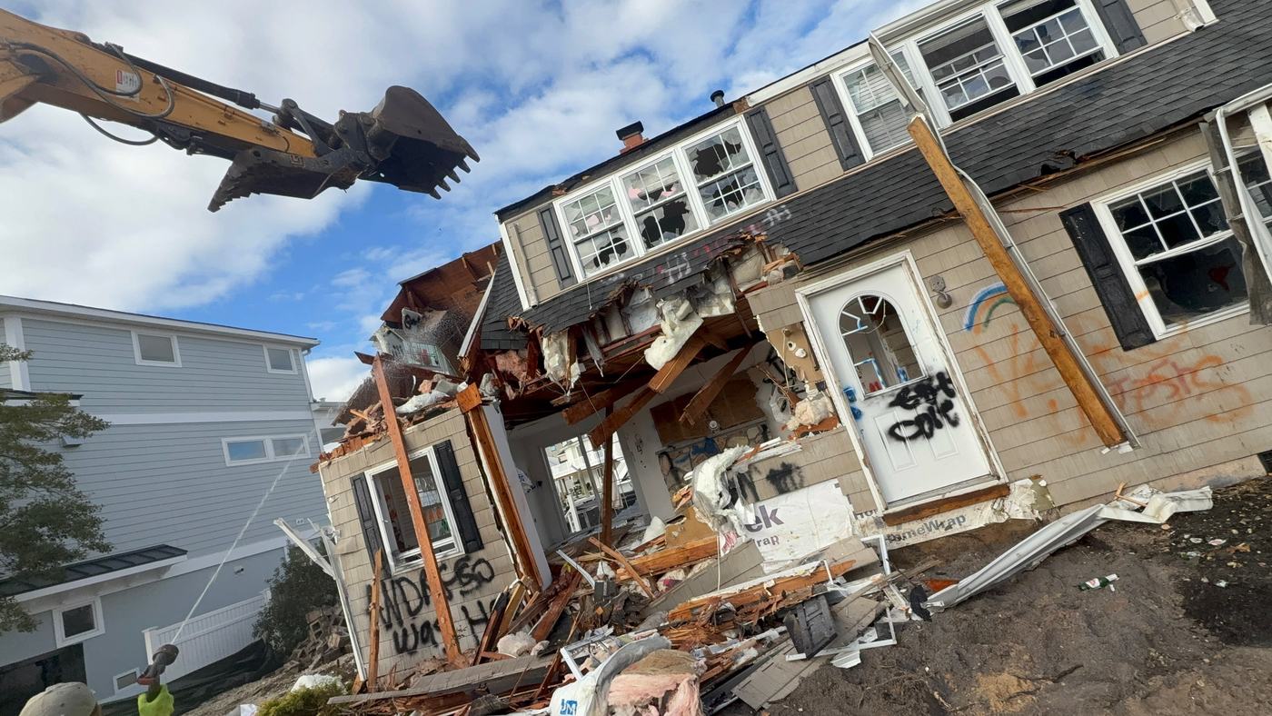 The front of a house collapsing inward during demolition with debris contained on the lot