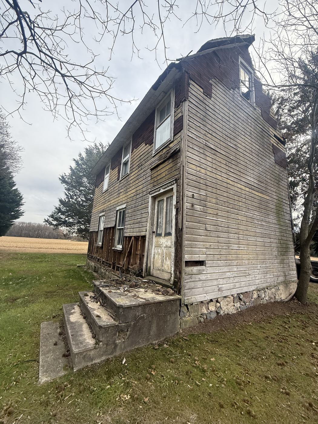 An abandoned wood frame farmhouse with weathered clapboard siding standing in a rural field