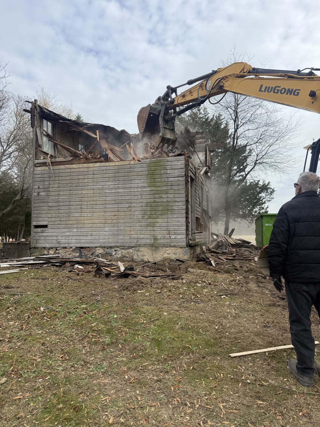 An excavator working the upper floor of an old farmhouse down to the siding line
