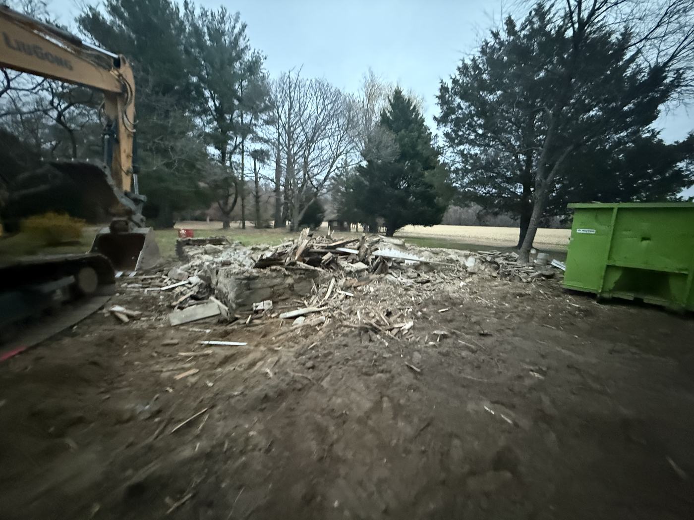 A cleared rural lot at dusk with the old stone foundation being worked out of the ground