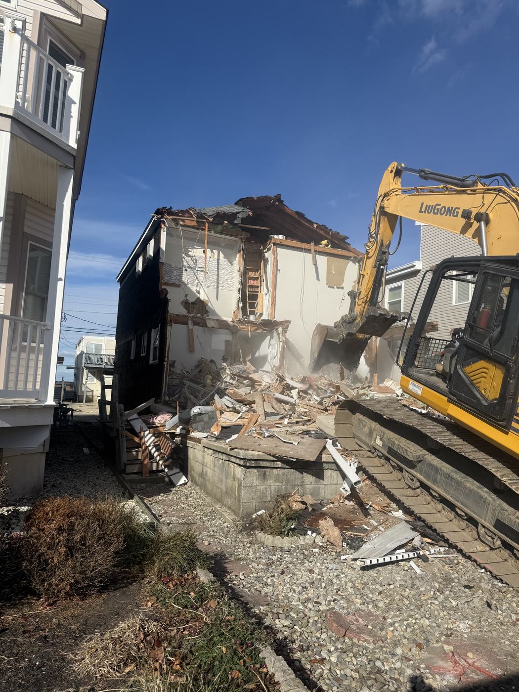 An excavator bucket working the open side of a partly demolished shore house