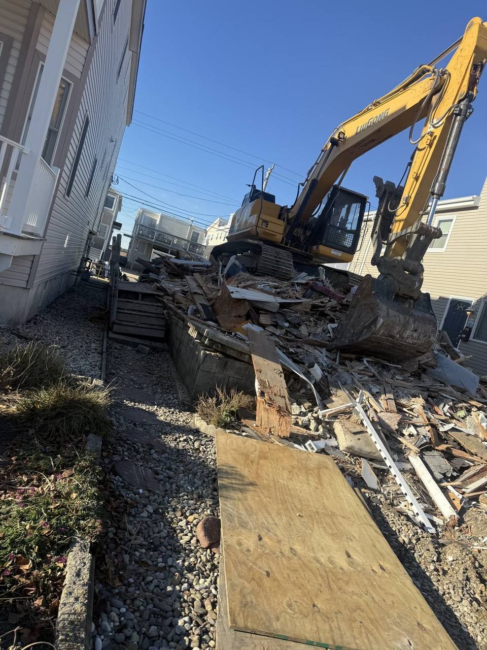 A demolition debris pile on a narrow lot with an excavator loading material