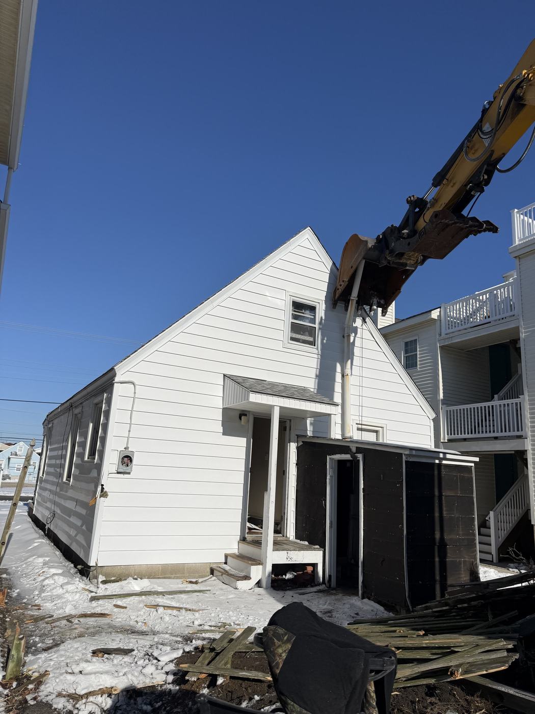 A white cape cod home standing before demolition with snow on the ground