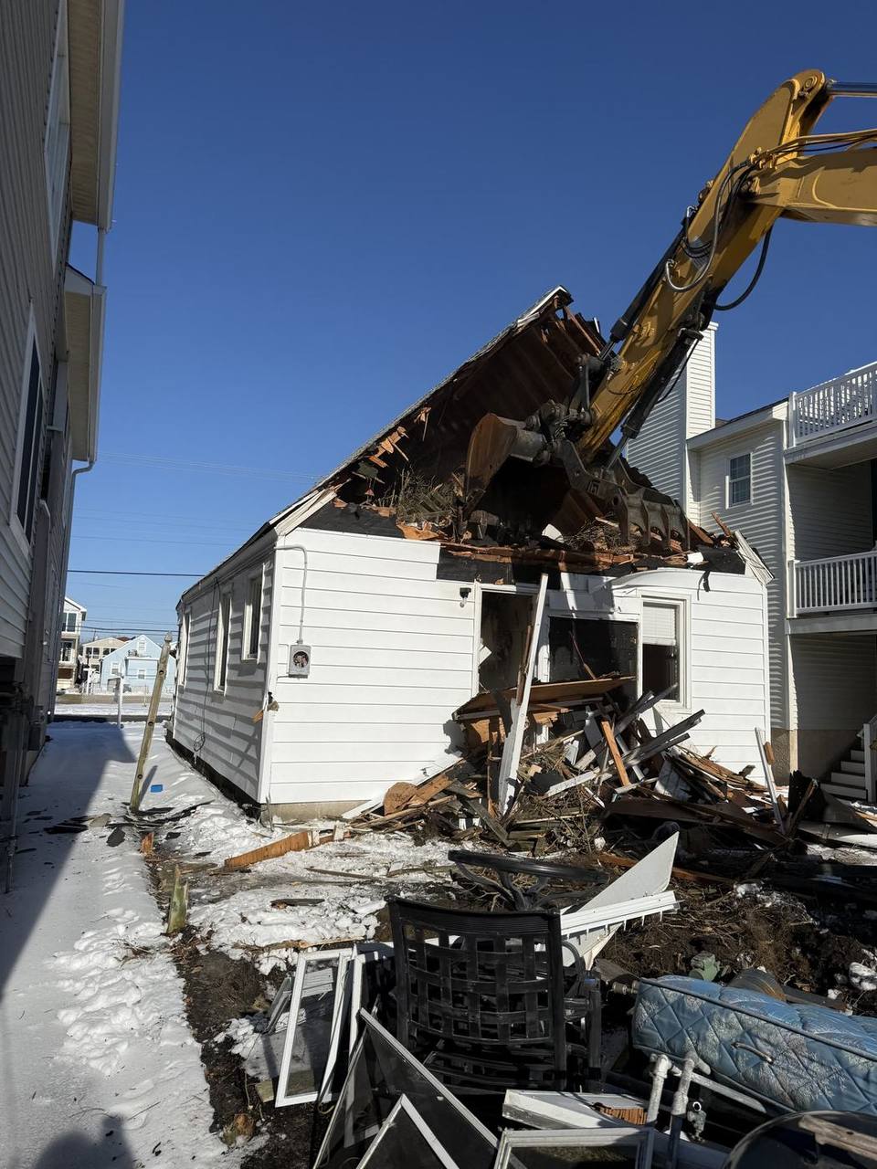 An excavator opening the roof of a single story house during a winter demolition