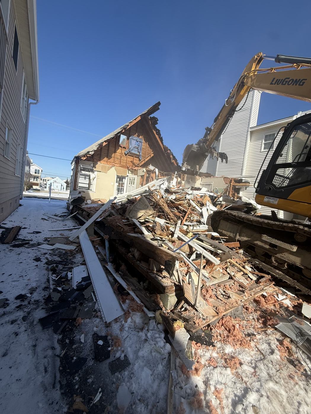 A cape cod home collapsed into a debris pile with the excavator working alongside
